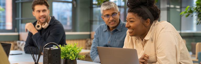 Picture of 3 people sat in a meeting, one is on their laptop